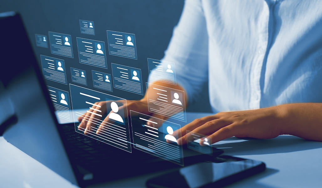 A user works on a laptop, with digital profile cards of patients.