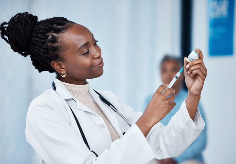 Hand wearing medical gloves and holding a needle syringe.