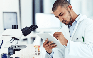 Healthcare professional working on a tablet in front of a microscope.