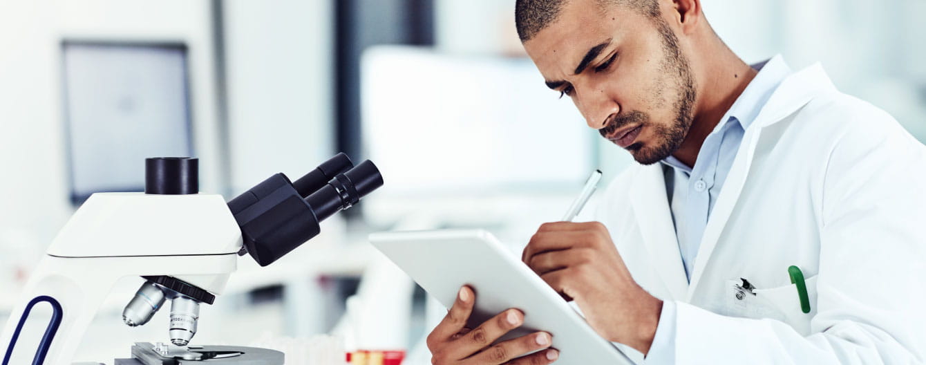 Healthcare professional working on a tablet in front of a microscope.