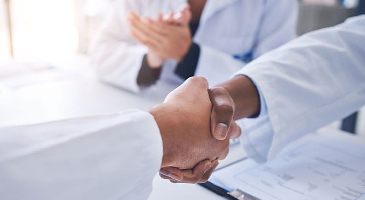 Doctors in white coats shake hands.