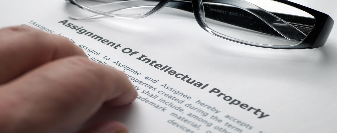 Image showing an assignment of intellectual property printed on a paper with a hand on top of it and an eyeglass.