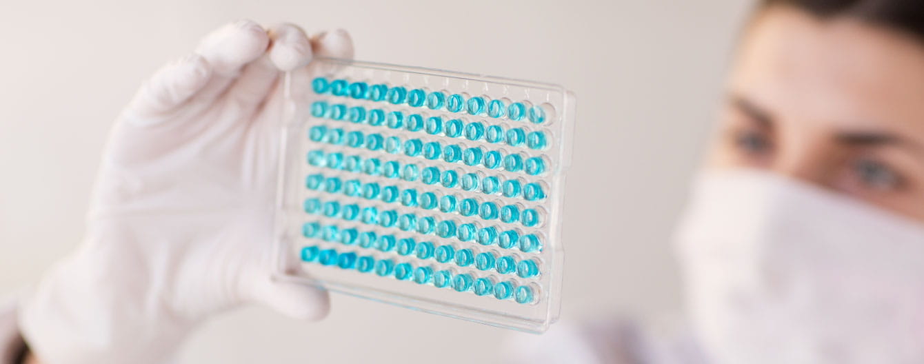 Woman in lab coat holding up test tube in research facility.