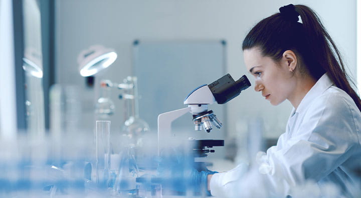 Young female researcher working in the lab, examining samples under a microscope