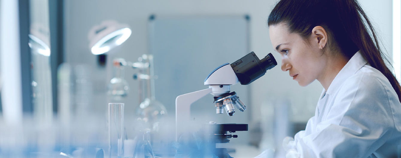 Young female researcher working in the lab, examining samples under a microscope