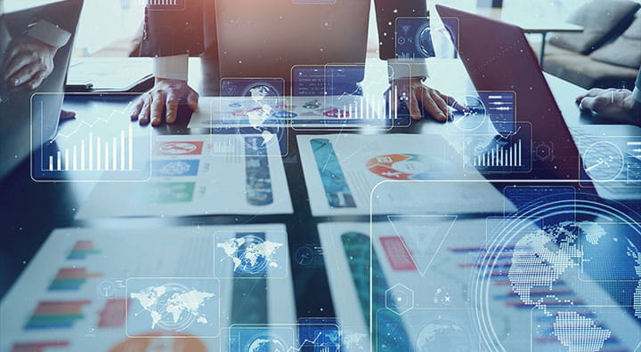 Business professionals analyze graphs and charts on a table, with digital data overlays and laptops in an office setting.