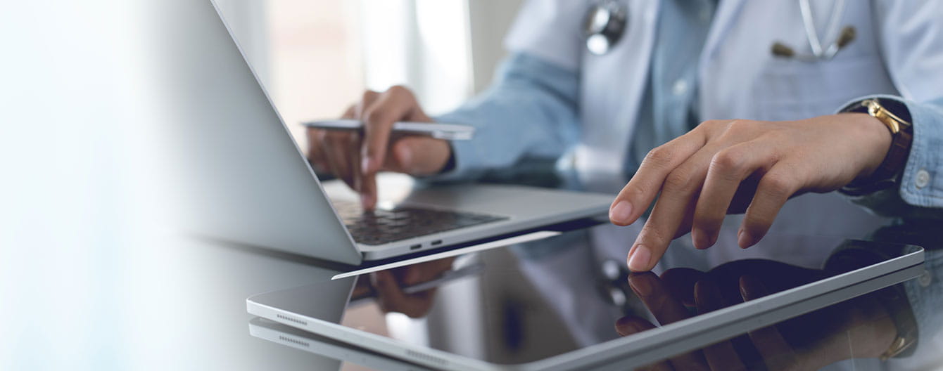 Doctor using digital tablet and working on laptop computer at doctor's office in hospital