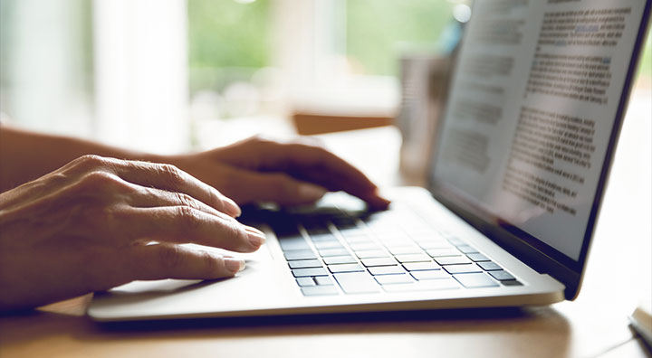 Medical writing expert typing on a laptop keyboard with a blurred document on the screen.