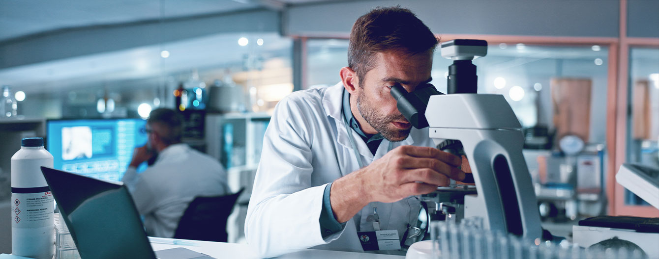 A male scientist in lab coat looking through a microscope.