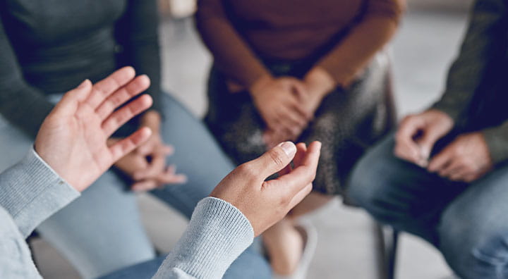 A close-up of hands engaged in conversation within a small group setting, with participants seated and focusing on dialogue.