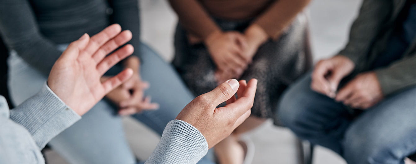A close-up of hands engaged in conversation within a small group setting, with participants seated and focusing on dialogue.