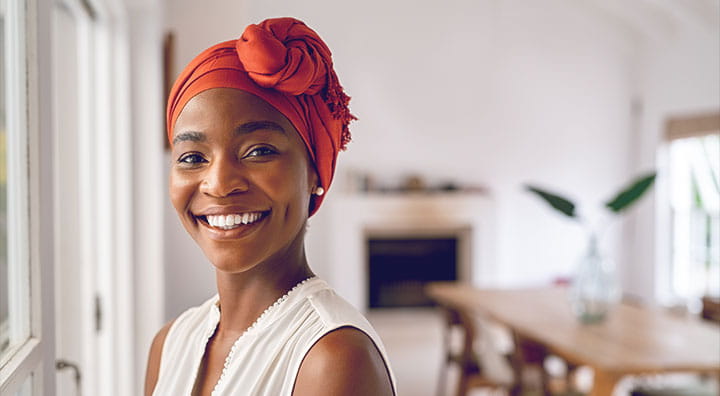 A woman wearing an orange head wrap stands in a bright room.