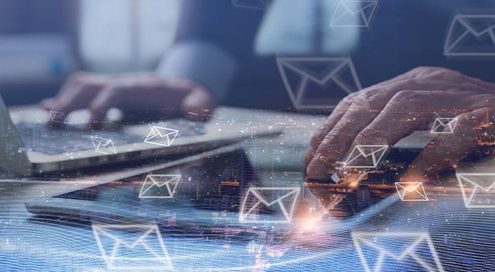 A person types on a laptop and tablet, surrounded by email icons.