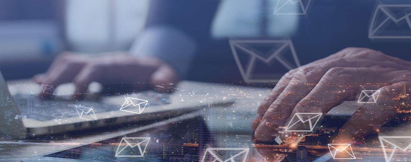 A person types on a laptop and tablet, surrounded by email icons.