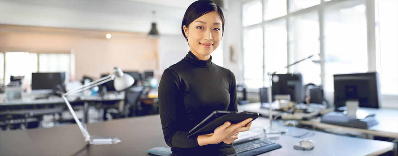 A person holds a tablet, standing in a modern office.