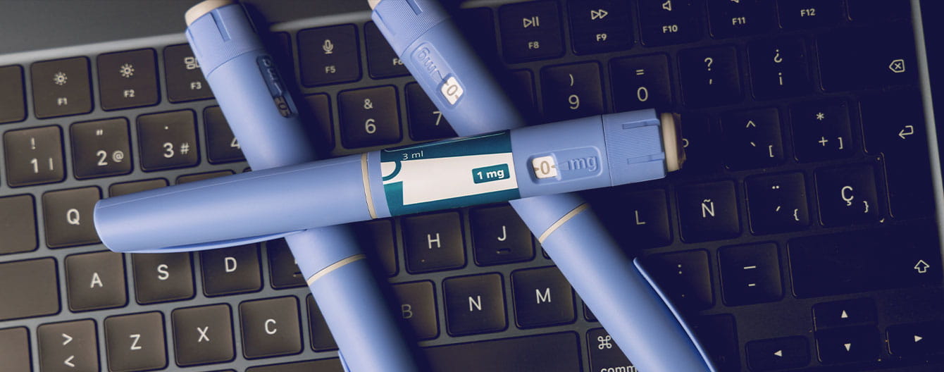 Blue medical injection pens are placed on a black laptop keyboard.