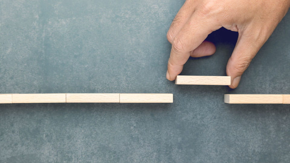 A conceptual image of a hand placing a wooden block to bridge a gap.