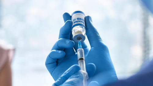 Healthcare professional withdrawing from a vial using a syringe.